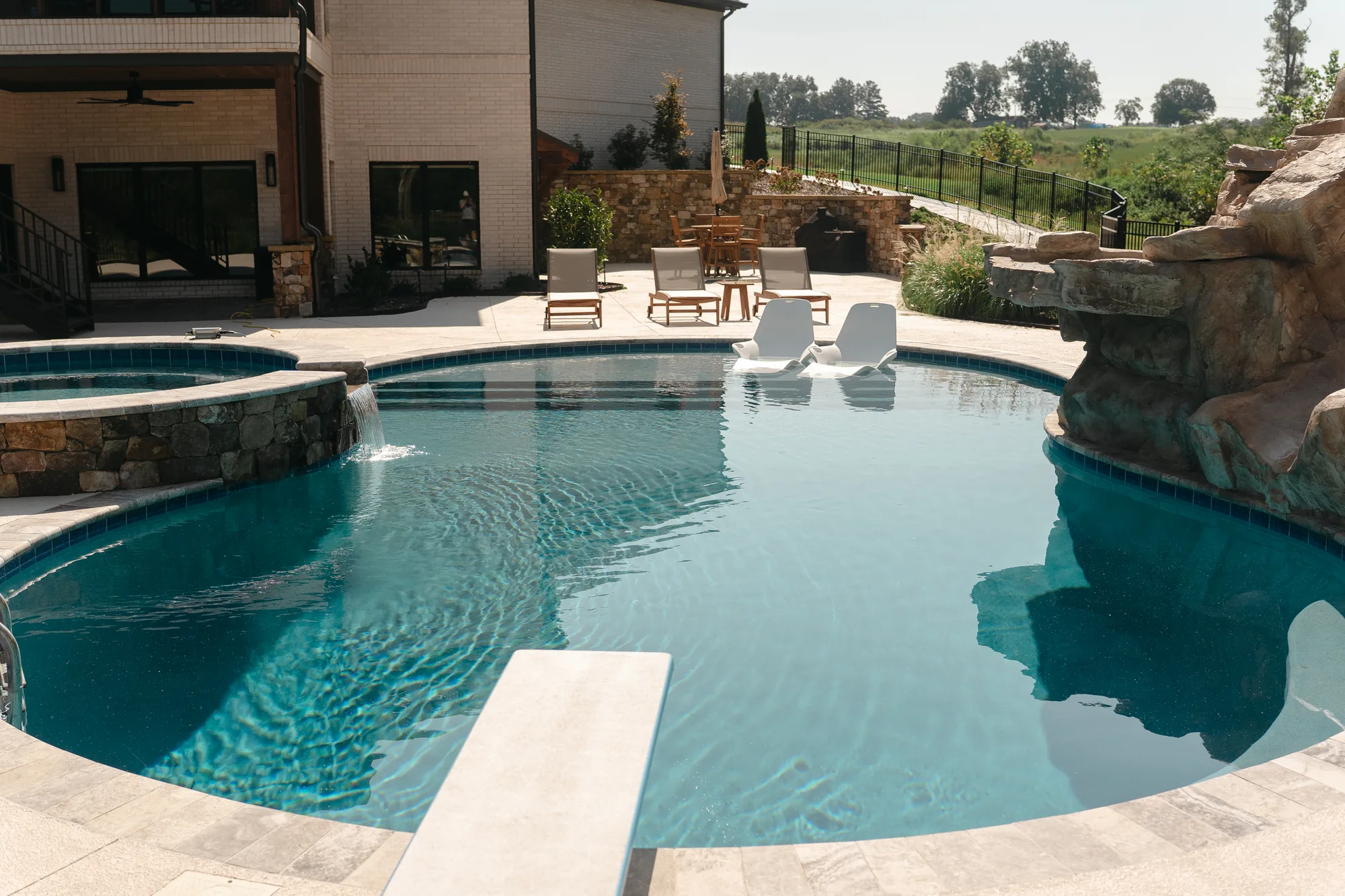 Freeform pool with a raised stone spa spilling into the water, tanning-ledge loungers and a diving board in Cullman, Alabama