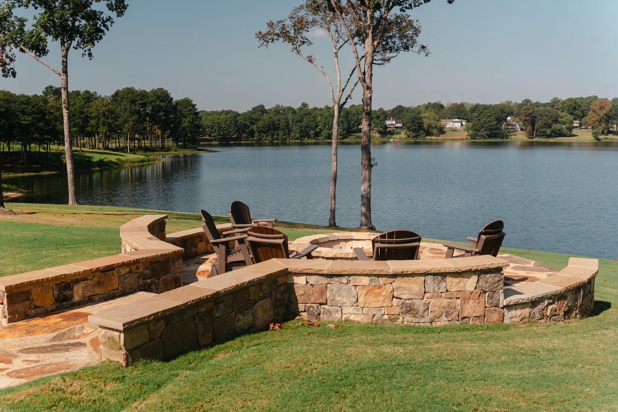 Lakeside stone fire pit with a curved seat wall and mortared flagstone patio overlooking Lake Catoma in Cullman, Alabama