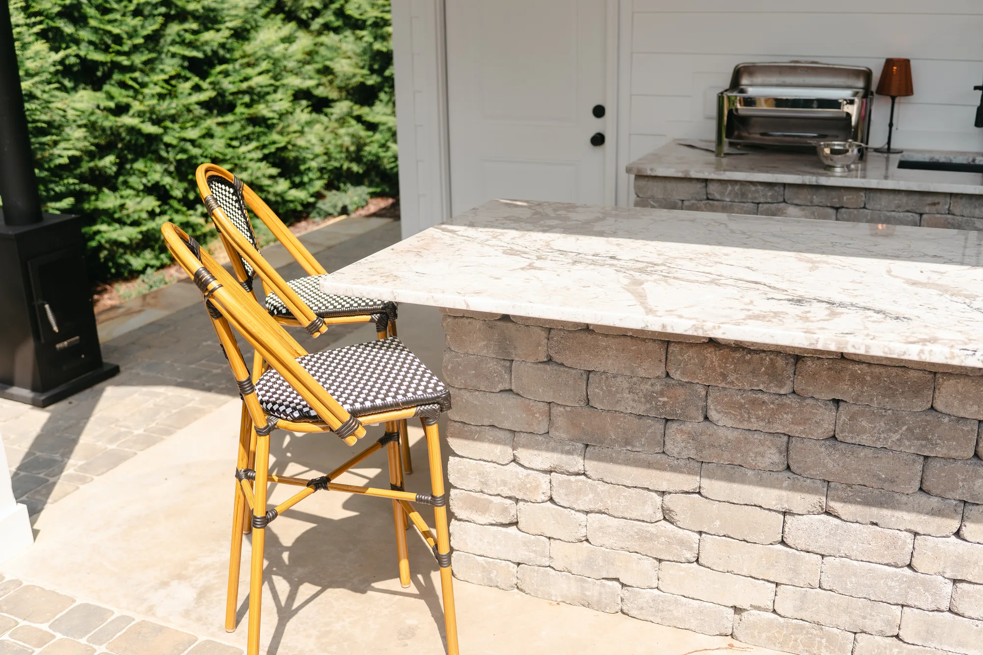 Stacked block outdoor kitchen island with a veined stone counter, rattan bar stools and a built-in grill in Madison, Alabama