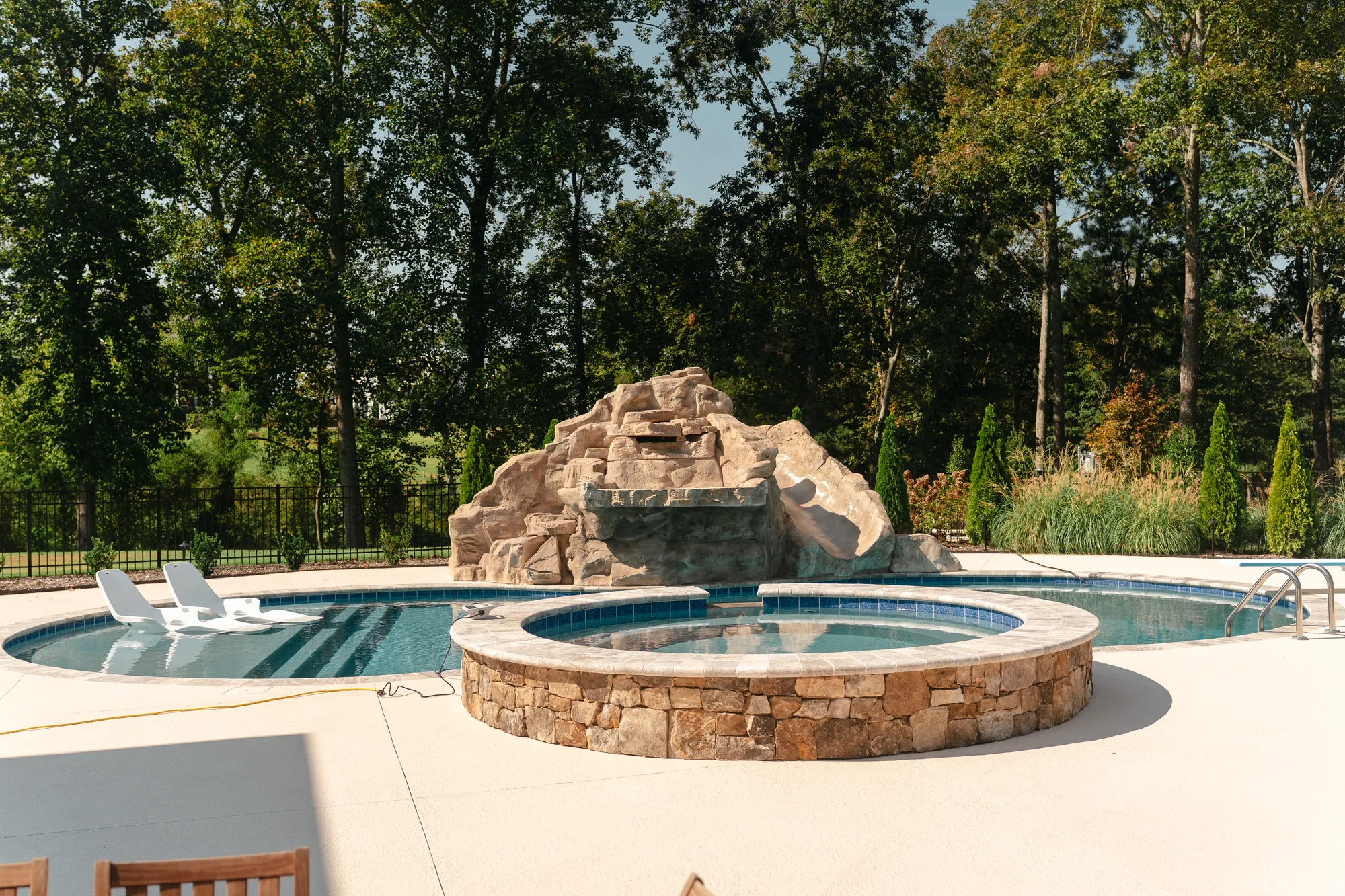 Pool with a sculpted rock grotto waterfall, round raised stone spa and tanning-ledge loungers in Cullman, Alabama