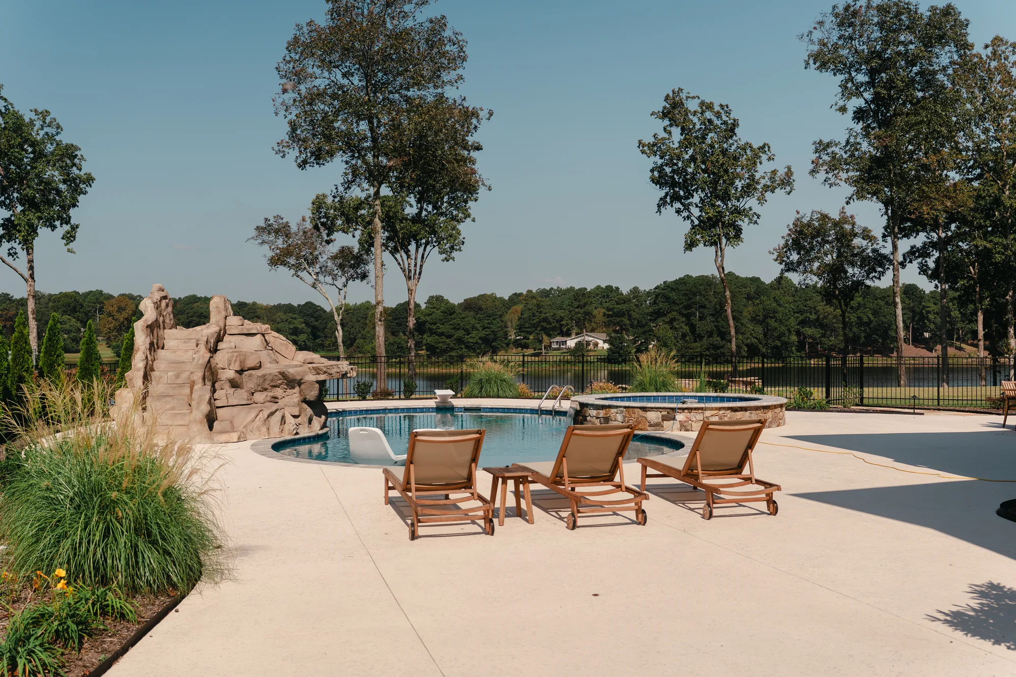 Poolside patio with teak loungers and ornamental grass plantings, rock slide and spa beyond, overlooking Lake Catoma in Cullman, Alabama