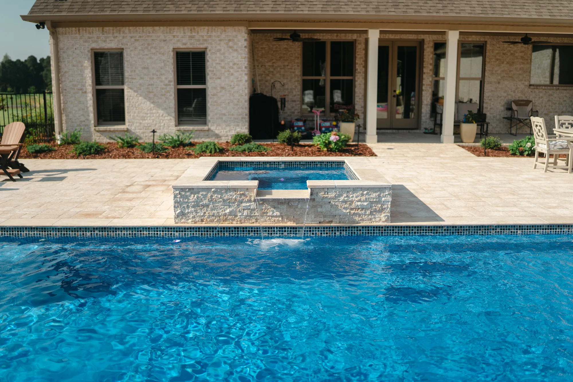 Rectangular pool with a square spillover spa and stacked stone water feature on a travertine deck in Guntersville, Alabama