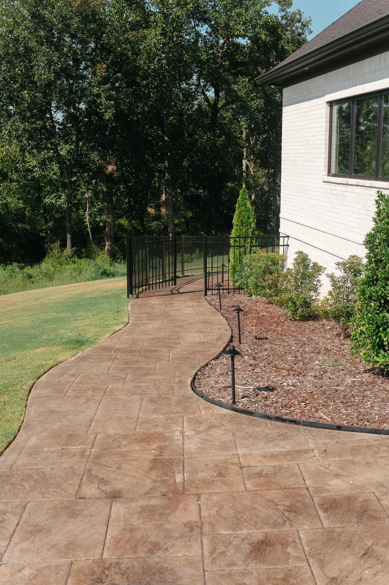 Curved stamped concrete walkway with mulched planting beds and path lighting alongside a brick home in Cullman, Alabama