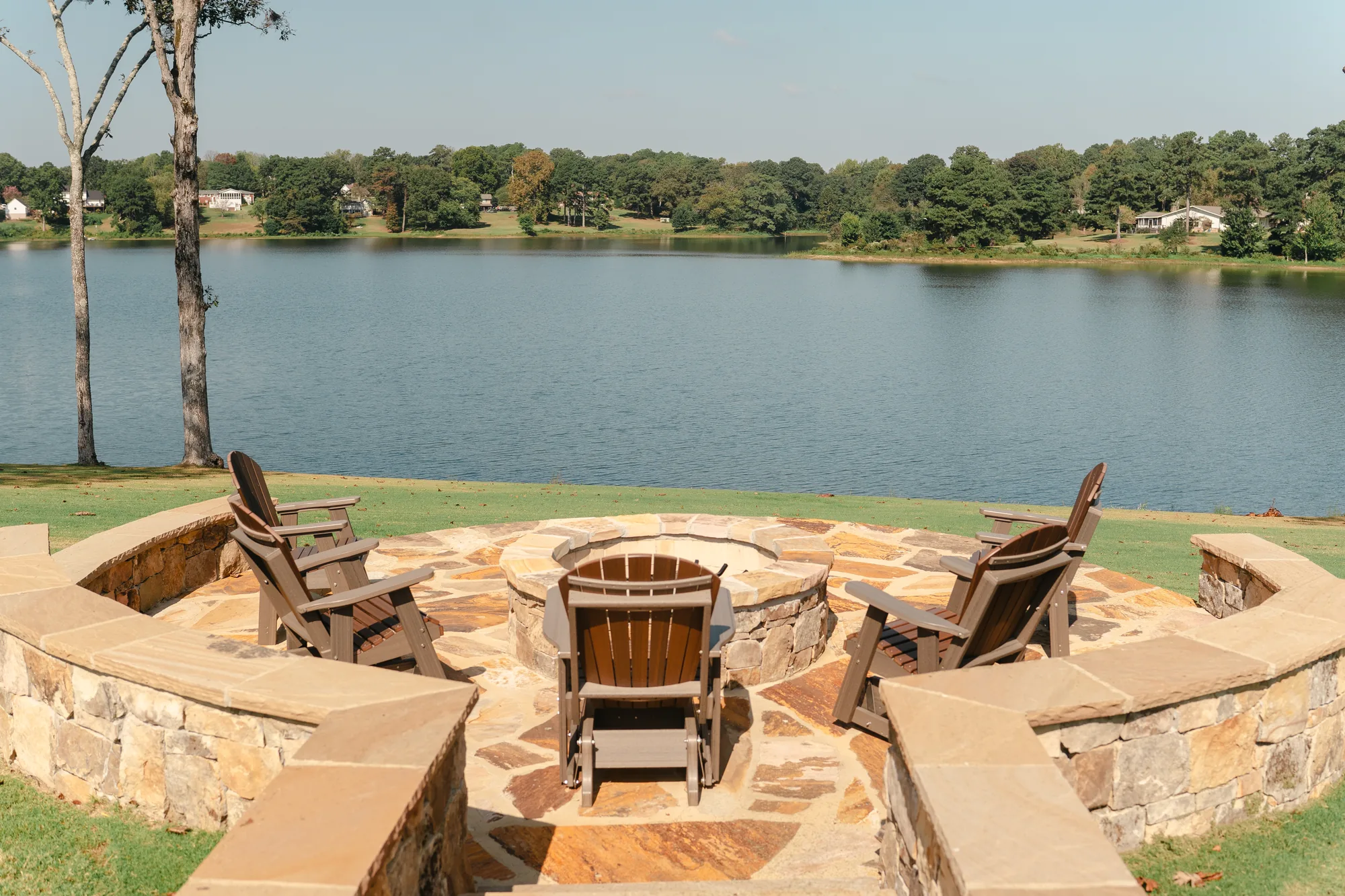 Round stone fire pit ringed by Adirondack chairs and a curved stone seat wall at the edge of Lake Catoma in Cullman, Alabama