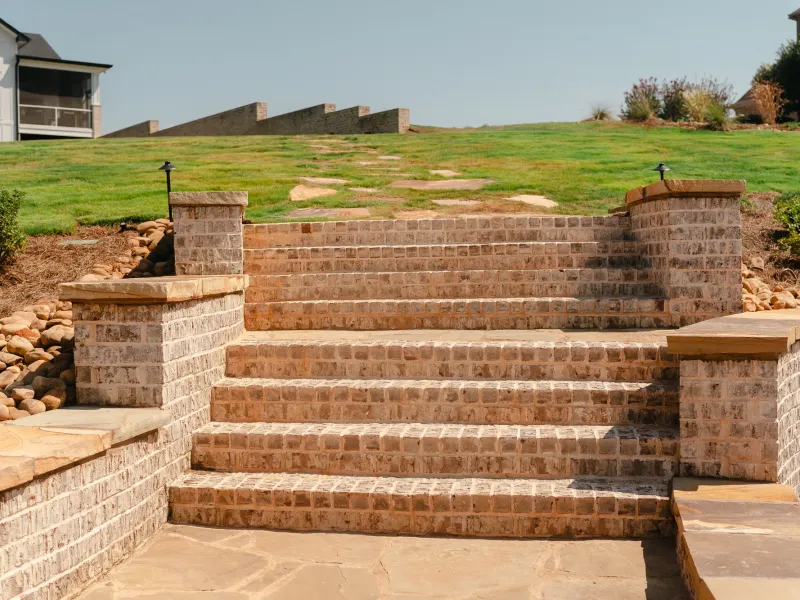 Wide brick steps with sandstone caps between brick retaining walls, with a river-rock dry creek bed and a flagstone landing, in Athens, Alabama