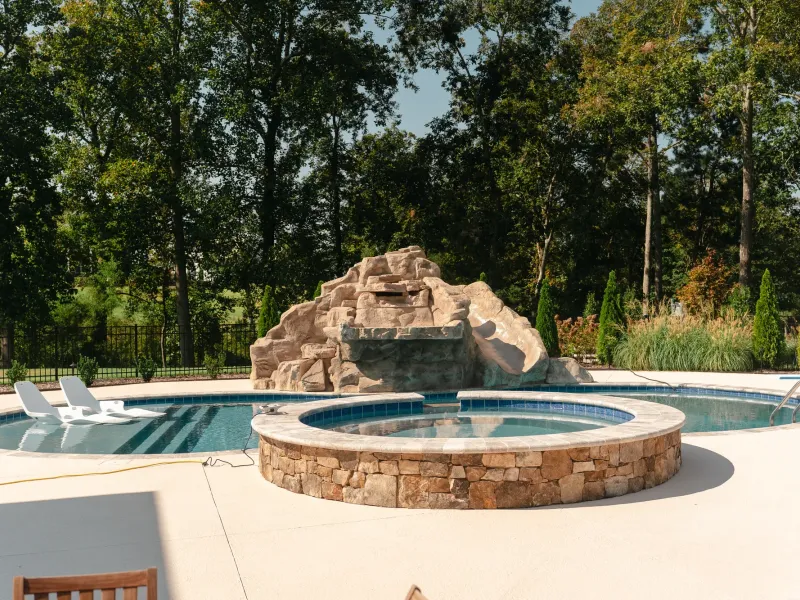 Pool with a sculpted rock grotto waterfall, round raised stone spa and tanning-ledge loungers in Cullman, Alabama