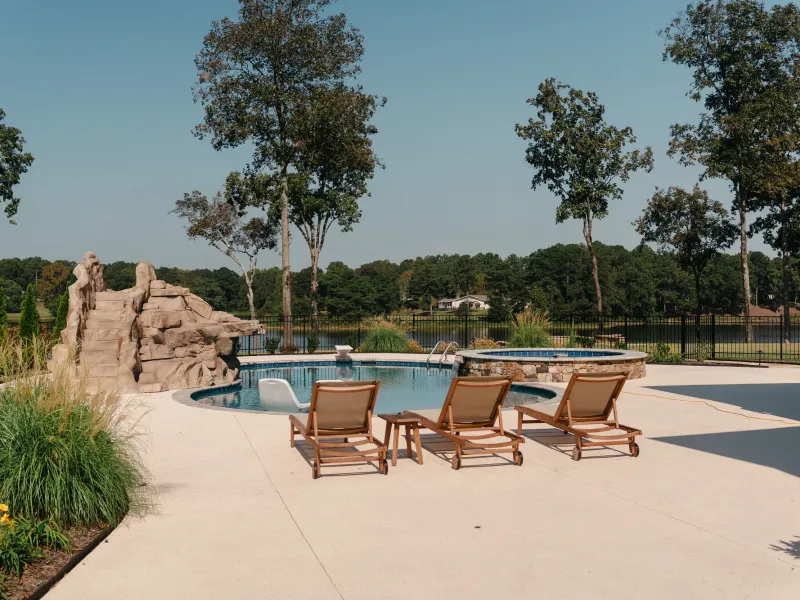 Poolside patio with teak loungers and ornamental grass plantings, rock slide and spa beyond, overlooking Lake Catoma in Cullman, Alabama