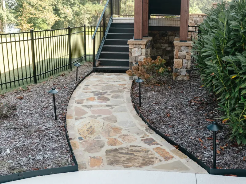 Mortared flagstone walkway lit by black path lights, running between mulch beds from a patio to the stairs of a stone-columned deck in Cullman, Alabama