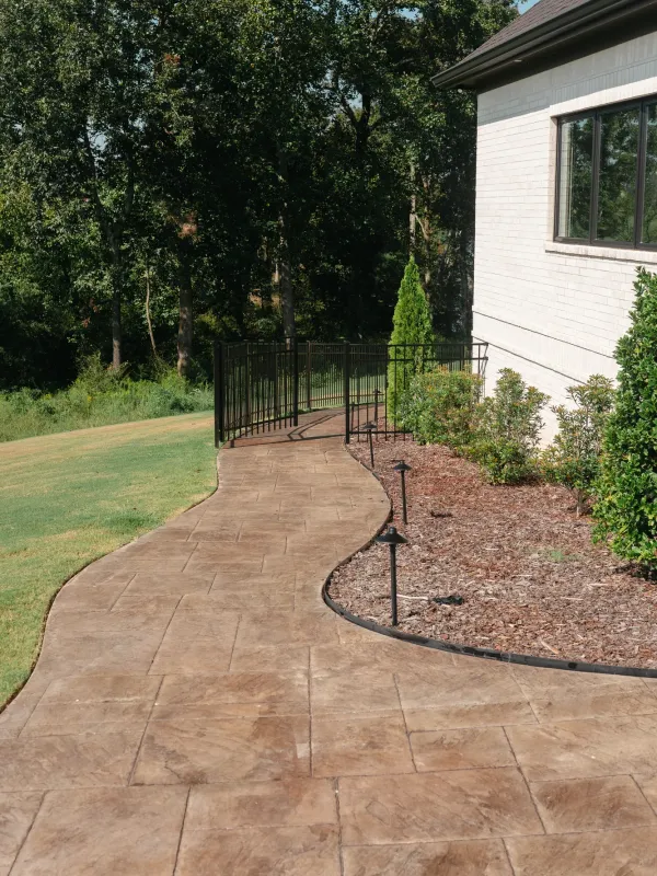 Curved stamped concrete walkway with mulched planting beds and path lighting alongside a brick home in Cullman, Alabama