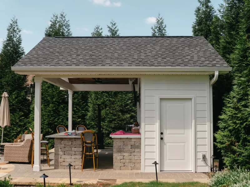 White pool house with a covered outdoor kitchen bay and bar seating, screened by a row of arborvitae in Madison, Alabama