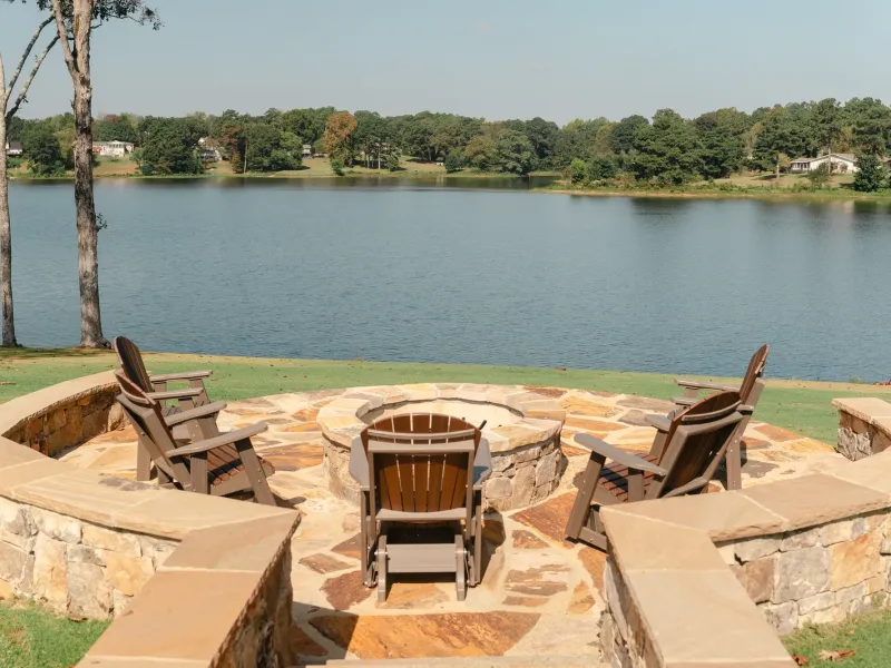 Round stone fire pit ringed by Adirondack chairs and a curved stone seat wall at the edge of Lake Catoma in Cullman, Alabama