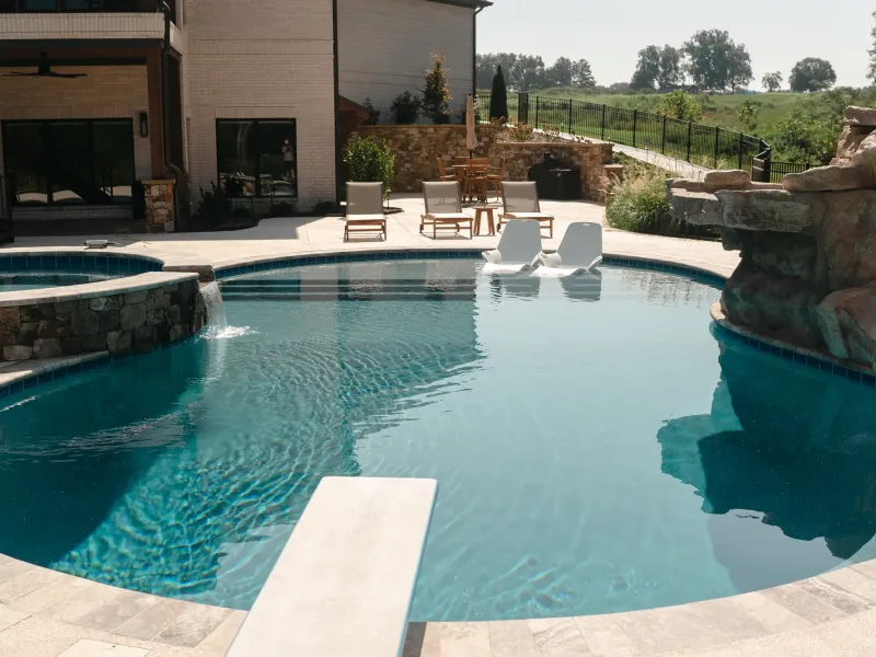 Freeform pool with a raised stone spa spilling into the water, tanning-ledge loungers and a diving board in Cullman, Alabama